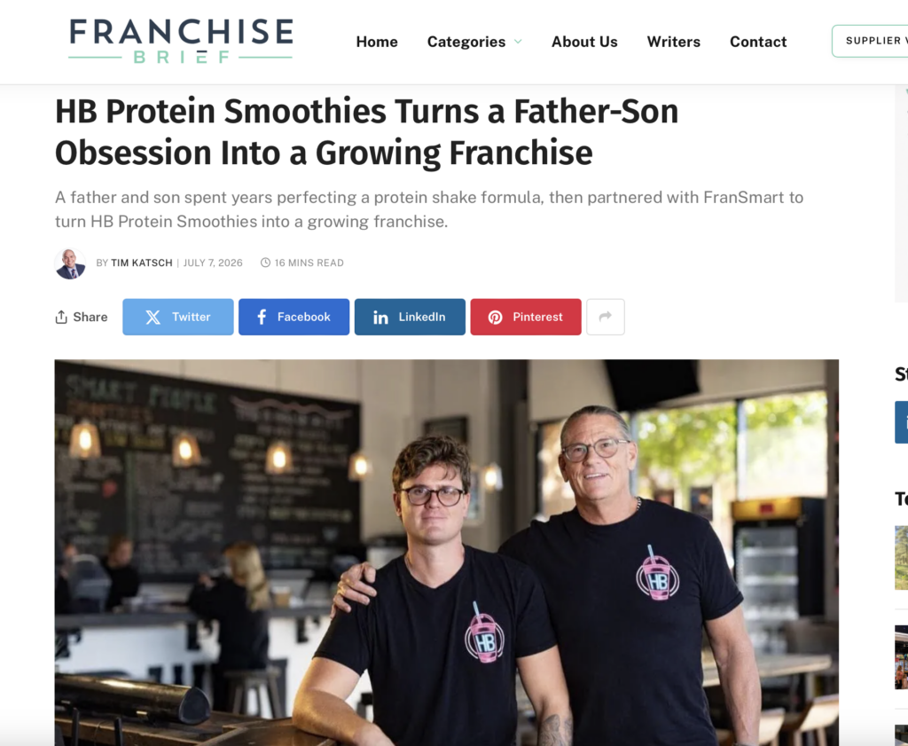 Two men wearing black HB Protein Smoothies t-shirts inside a cafe with wooden tables and chalkboard menu